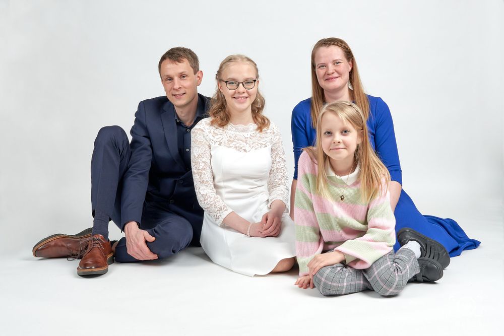 Family group portrait with four people wearing coordinated outfits on white background.