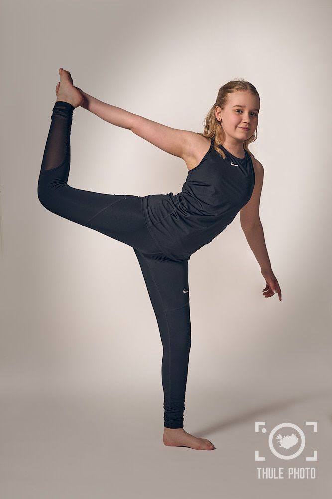 Athletic dancer in black workout gear performing a standing split pose against a white background.
