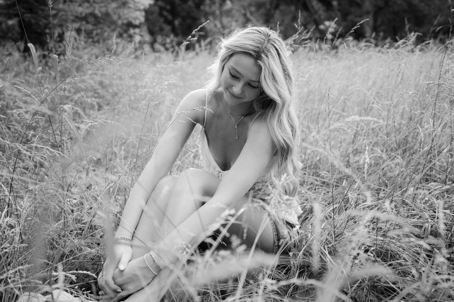 A woman in a romantic white dress sits gracefully in a blooming wildflower meadow during golden hour.