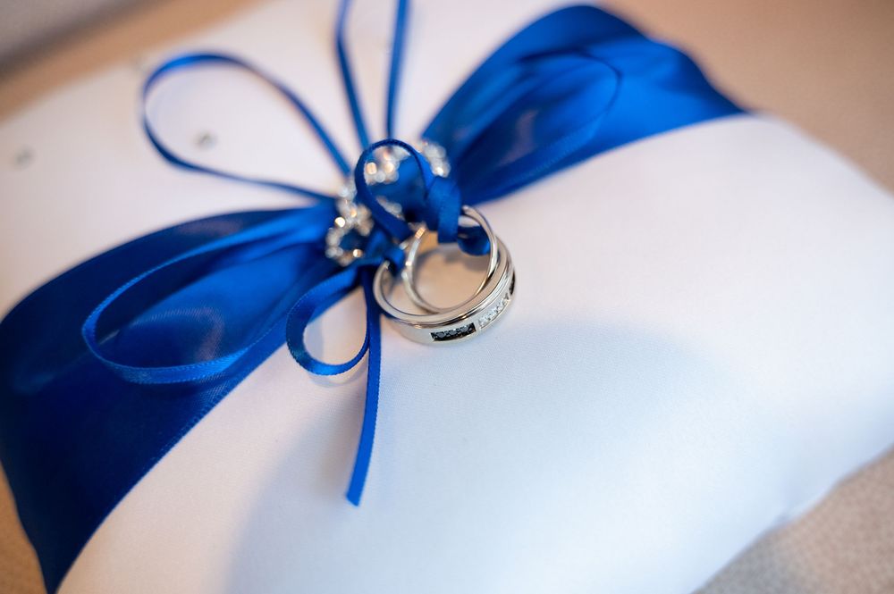 Navy blue satin wedding ring pillow sits with delicate lace detailing and a bow tied in an elegant knot.