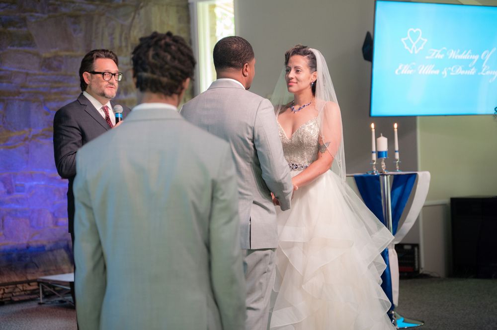 Wedding guests dance in celebration during a reception as purple and blue lighting illuminates the venue.