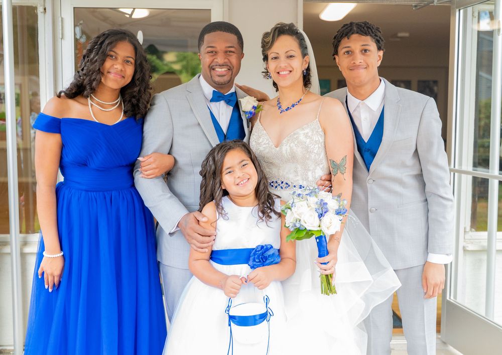 Wedding party in coordinated blue and gray attire poses together indoors for a formal portrait.