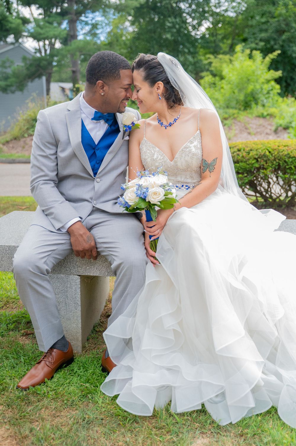 Couple in elegant wedding attire sharing intimate moments on garden benches surrounded by lush greenery.