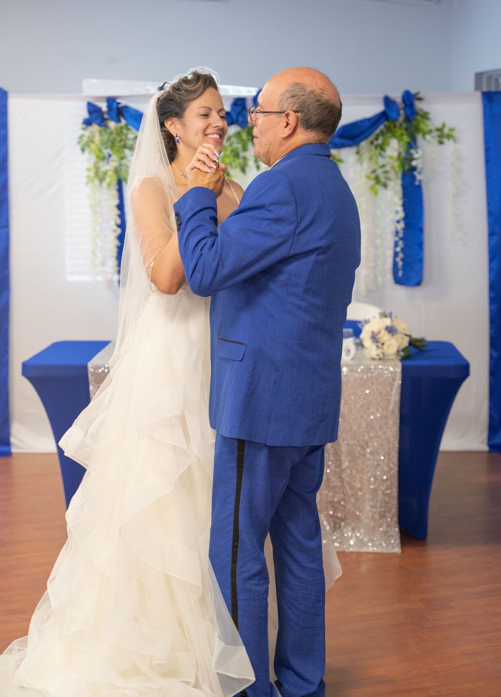 A couple shares an emotional dance moment at a wedding reception decorated with royal blue and silver accents.