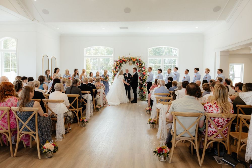 Elegant indoor wedding ceremony with floral arch and guests seated in wooden chairs.