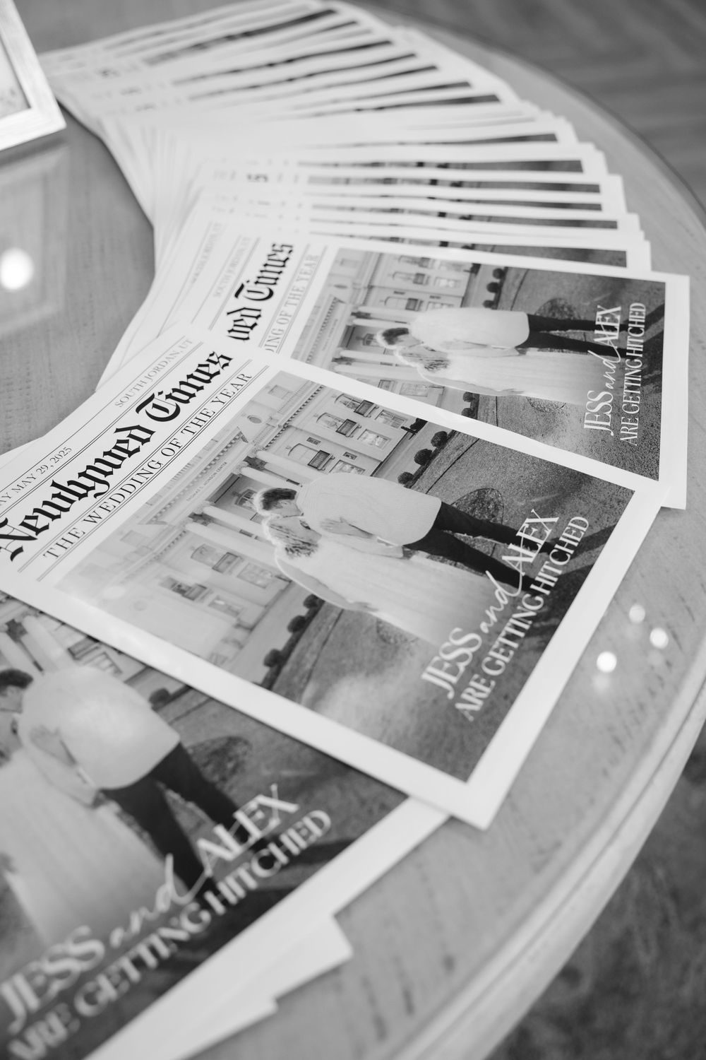 Black and white photo of Newlywed Times wedding newspapers fanned out on glass table.