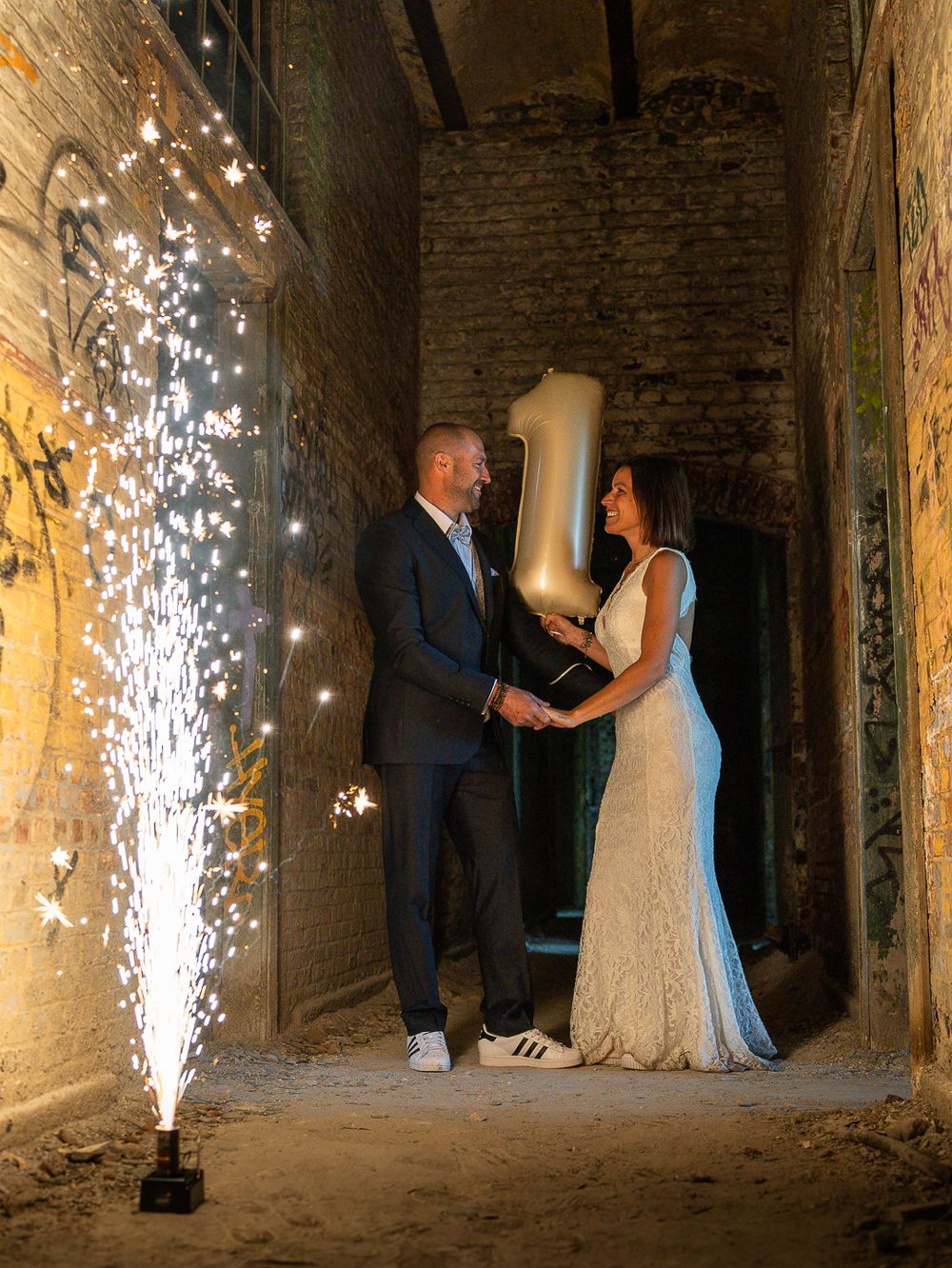 Un couple s'embrasse dans un passage pavé, sous des fontaines de feux d'artifice spectaculaires qui créent une atmosphère magique. Florent V