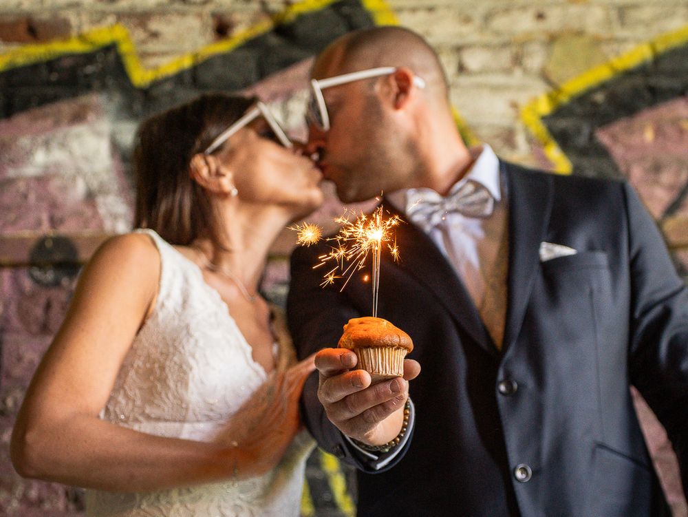 Couple romantique s'embrassant devant un mur couvert de graffitis, un cupcake décoré d'un cierge magique à la main. Florent Vause
