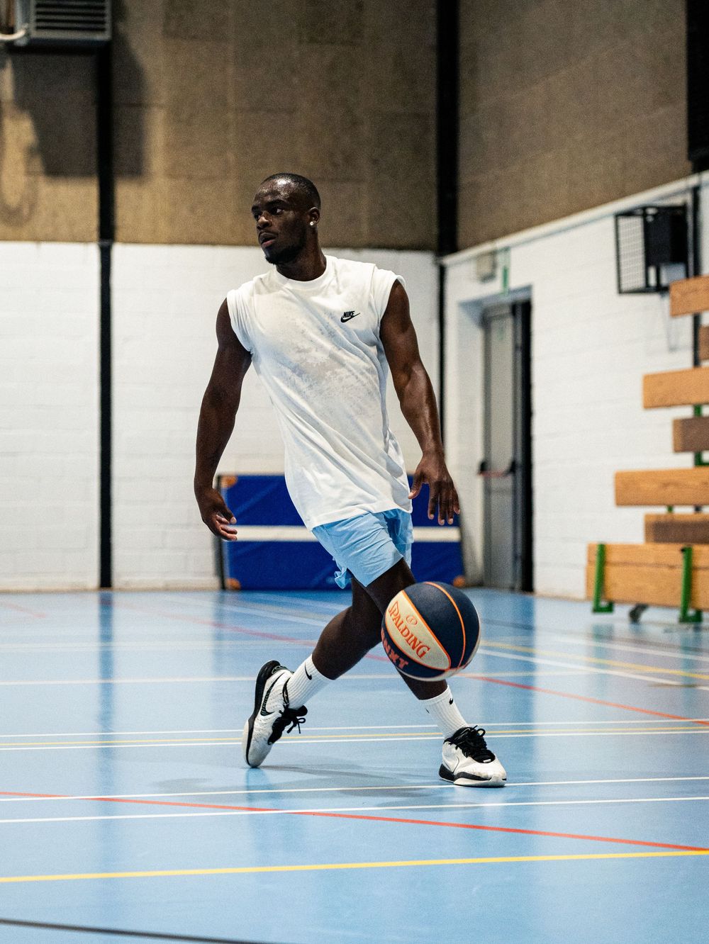 Joueur de basket-ball dribblant sur un terrain couvert, vêtu d'un maillot blanc et d'un short bleu. Florent Vause