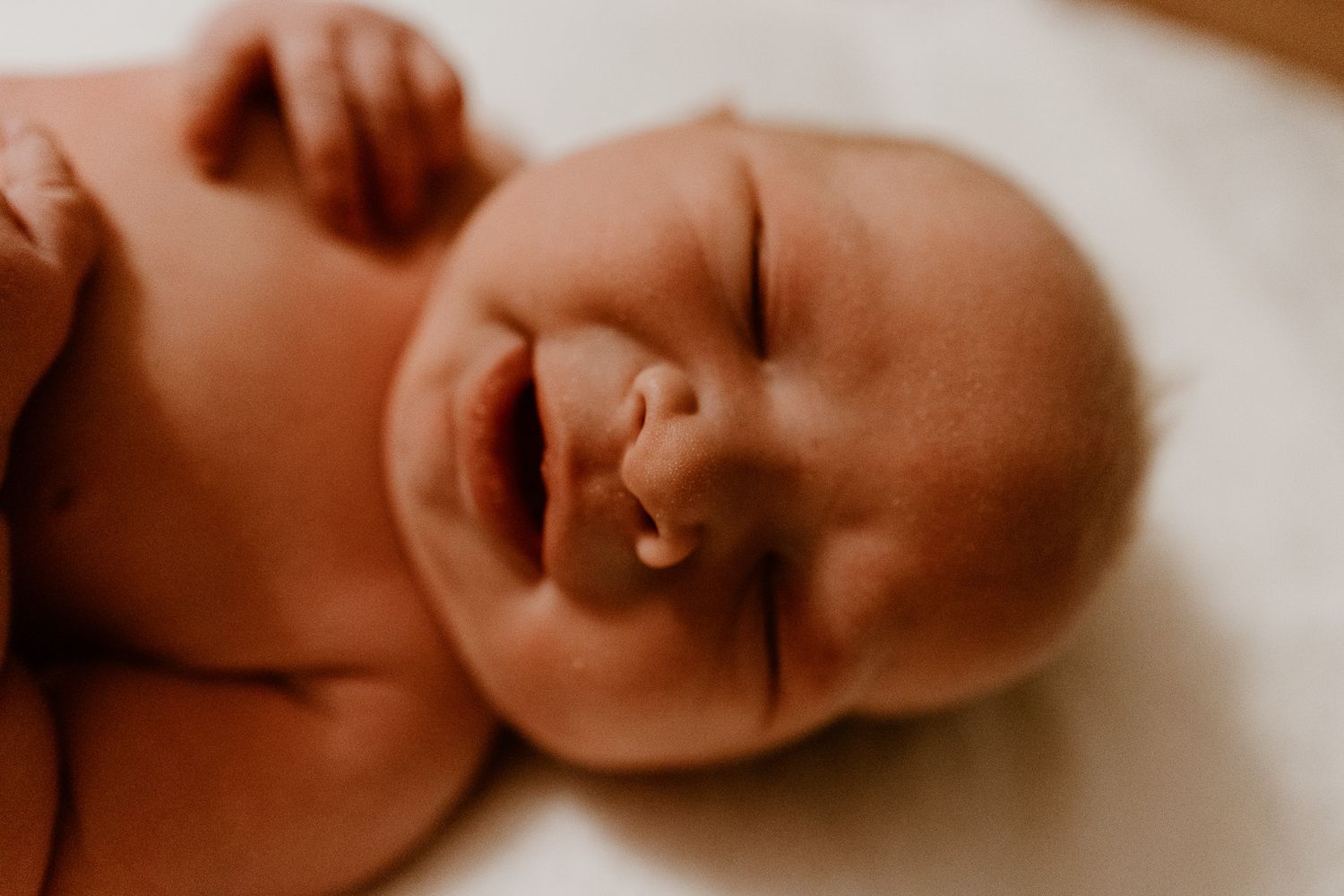 A peaceful sleeping baby laying down with a gentle smile and closed eyes in warm lighting.