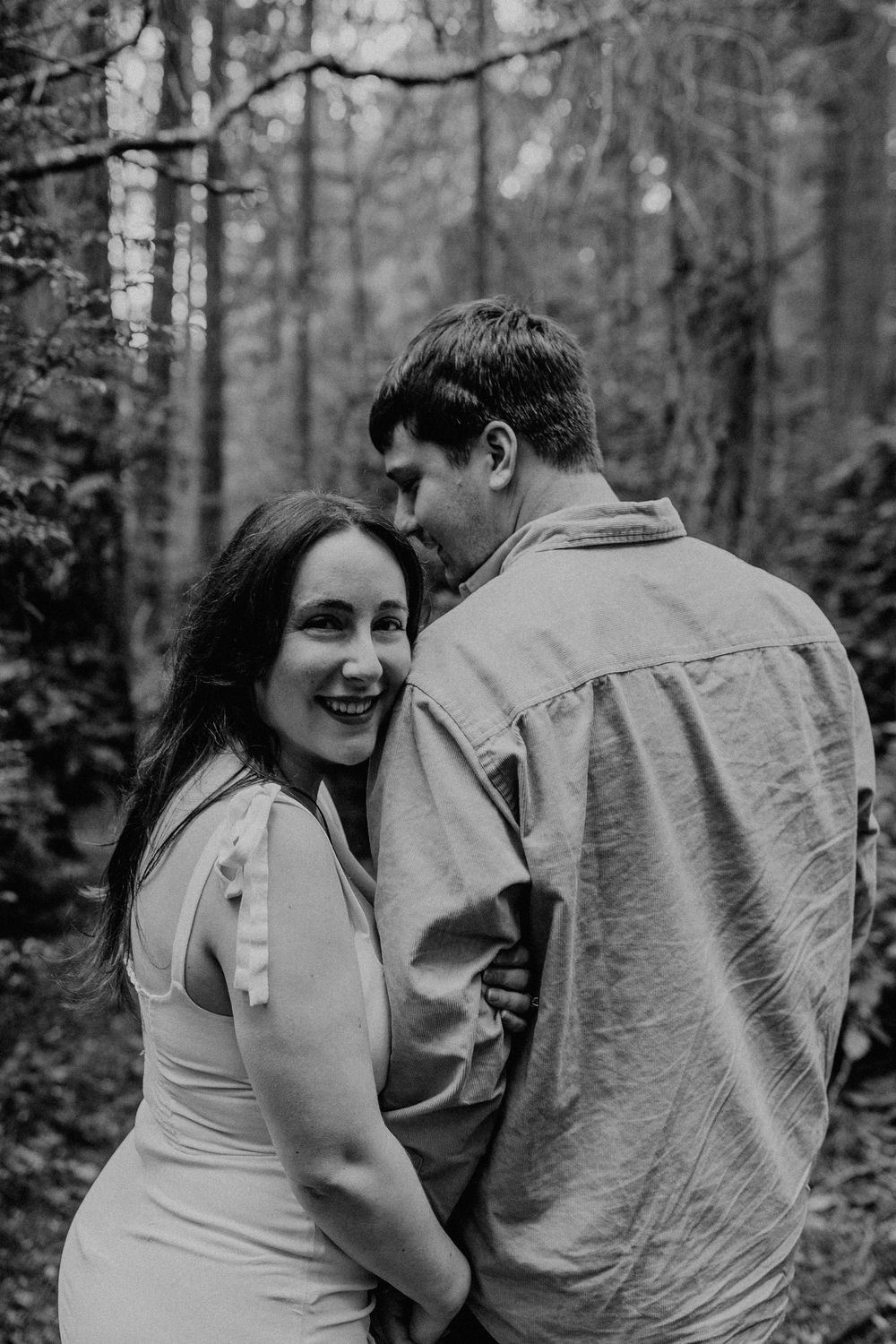 A romantic black and white portrait of a couple sharing an intimate moment in a misty forest.