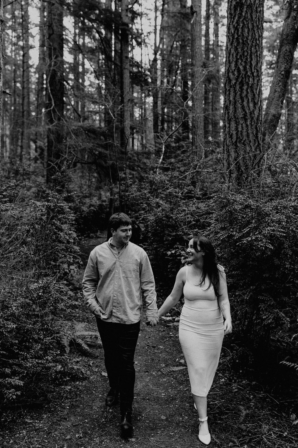 A couple walks together through a moody forest setting in black and white photography.