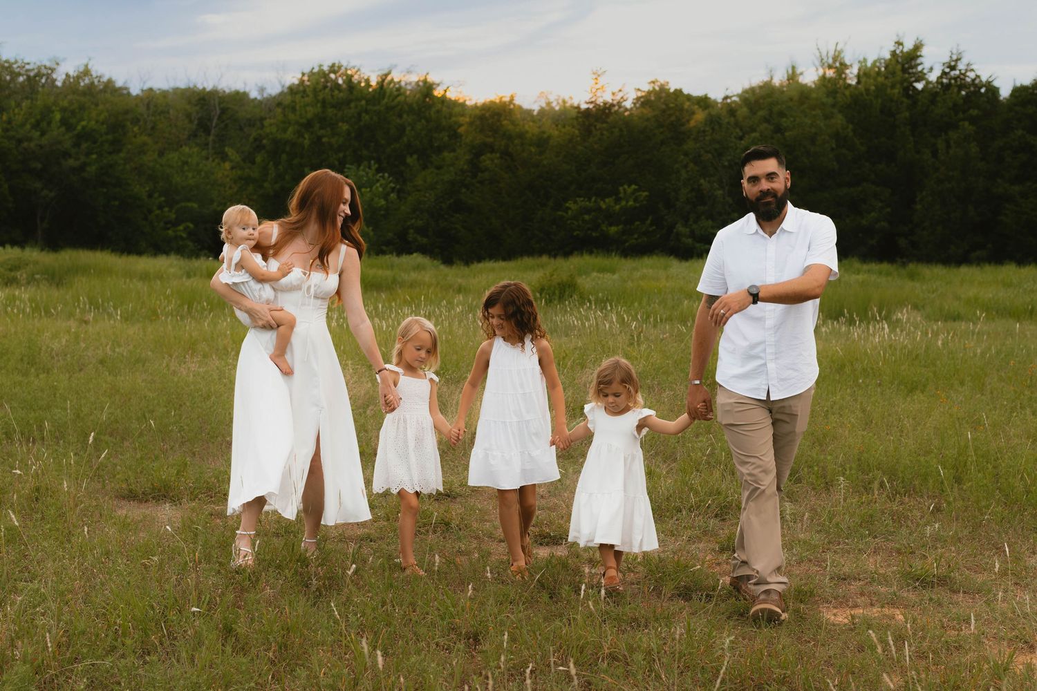 People in white clothing standing together in a grassy meadow with trees in the background on a sunny day.