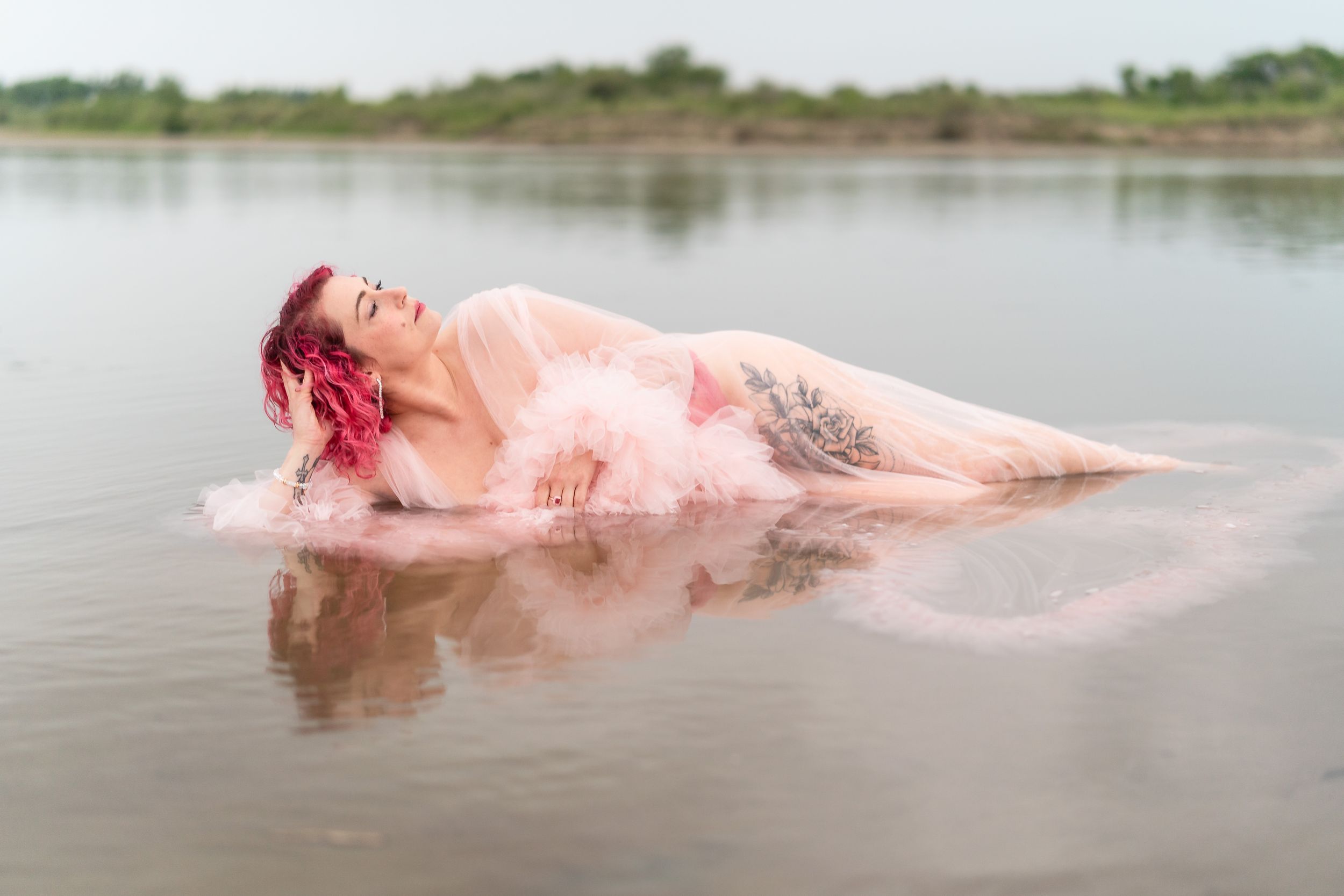 An ethereal water photography session shows a floating pink dress creating ripples across a tranquil lake.