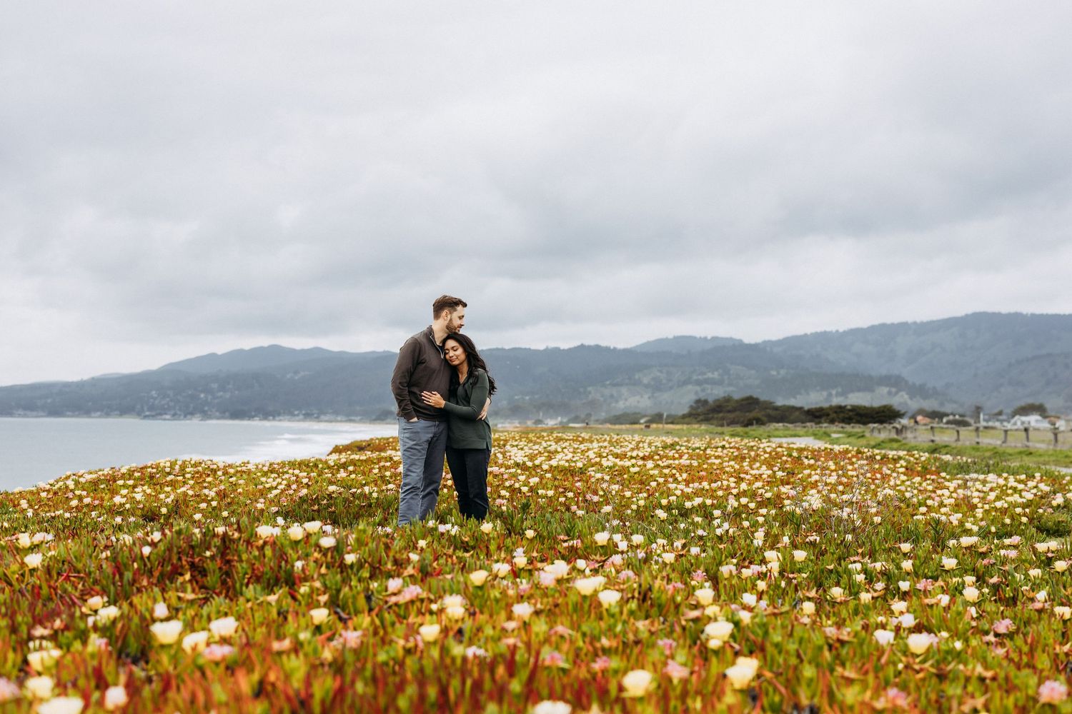 Bi-racial couple cuddles for engagement photos in Half Moon Bay