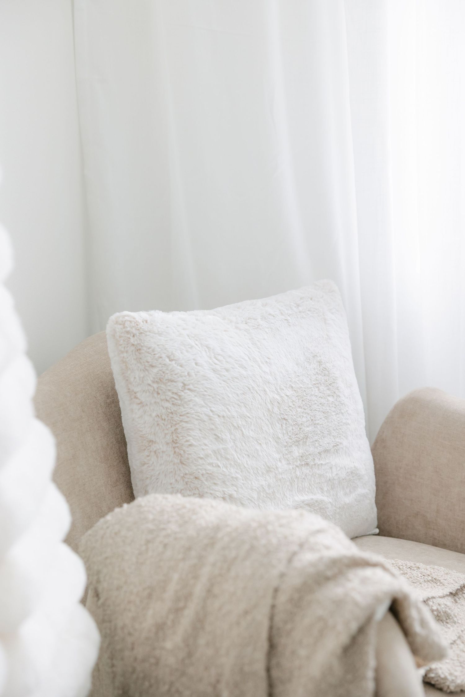 White throw pillows and sheer curtains create a soft, cozy corner in a neutral-toned living room.
