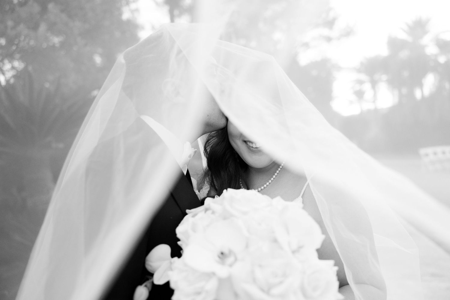 A romantic wedding couple poses against desert mountains and palm trees on a golf course with a flowing white dress and veil.