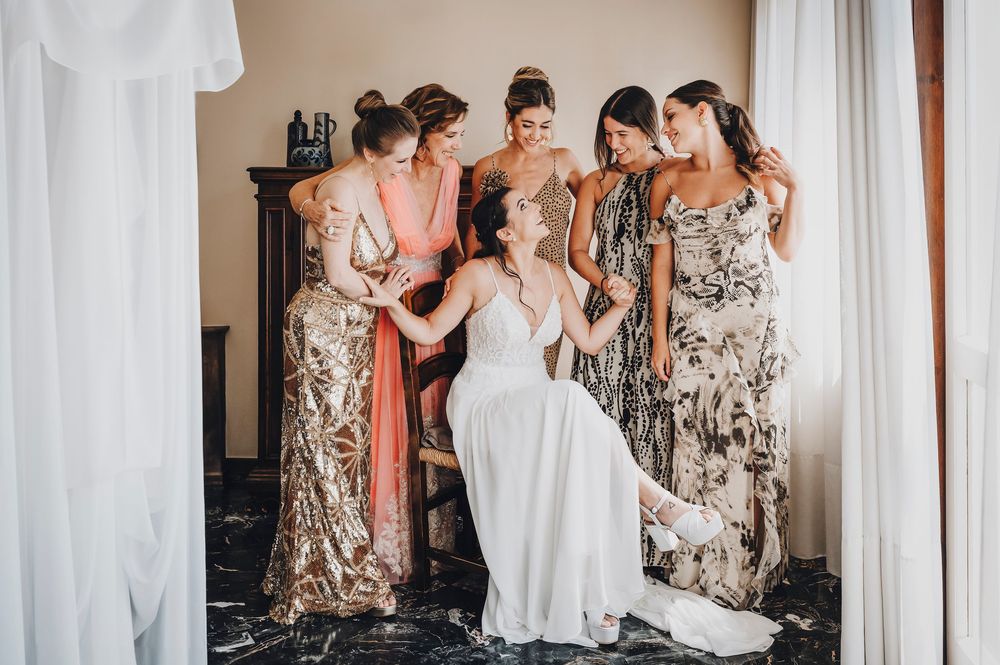 Festa di nozze: aiuto alla sposa nella preparazione in camera con abiti floreali.