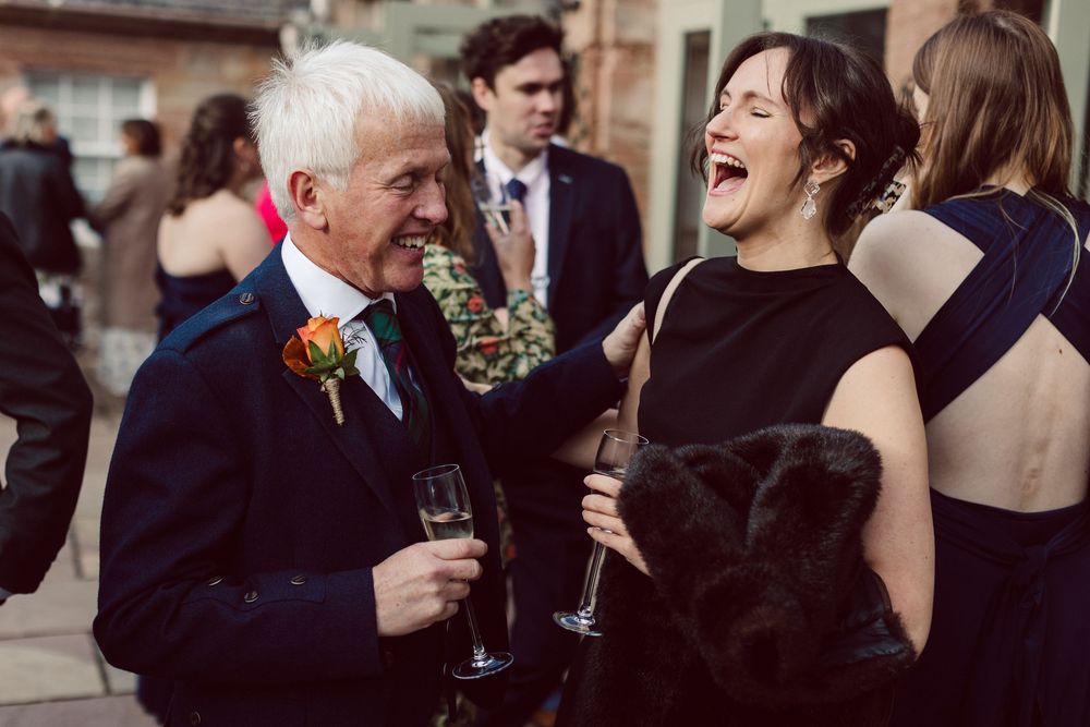 Wedding guests laugh and socialize while holding drinks at an outdoor reception celebration.