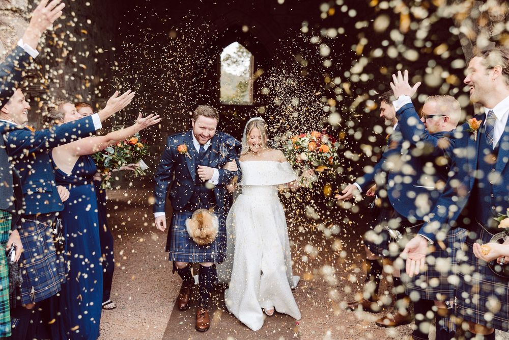 Newlyweds exit church celebration while guests throw confetti in joyful outdoor wedding celebration.