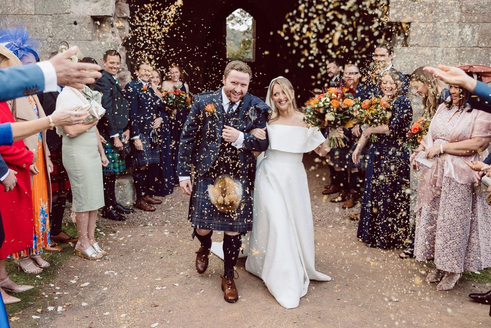 Wedding guests throw colorful confetti at a couple during their outdoor celebration.