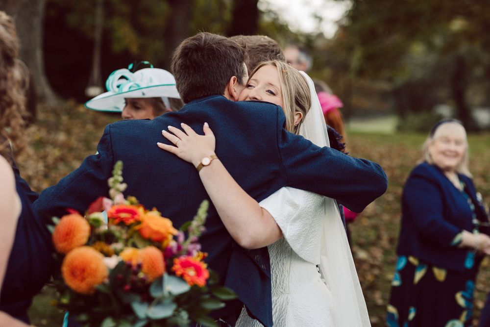 A wedding party celebrates outdoors with colorful orange and red floral arrangements in the background.