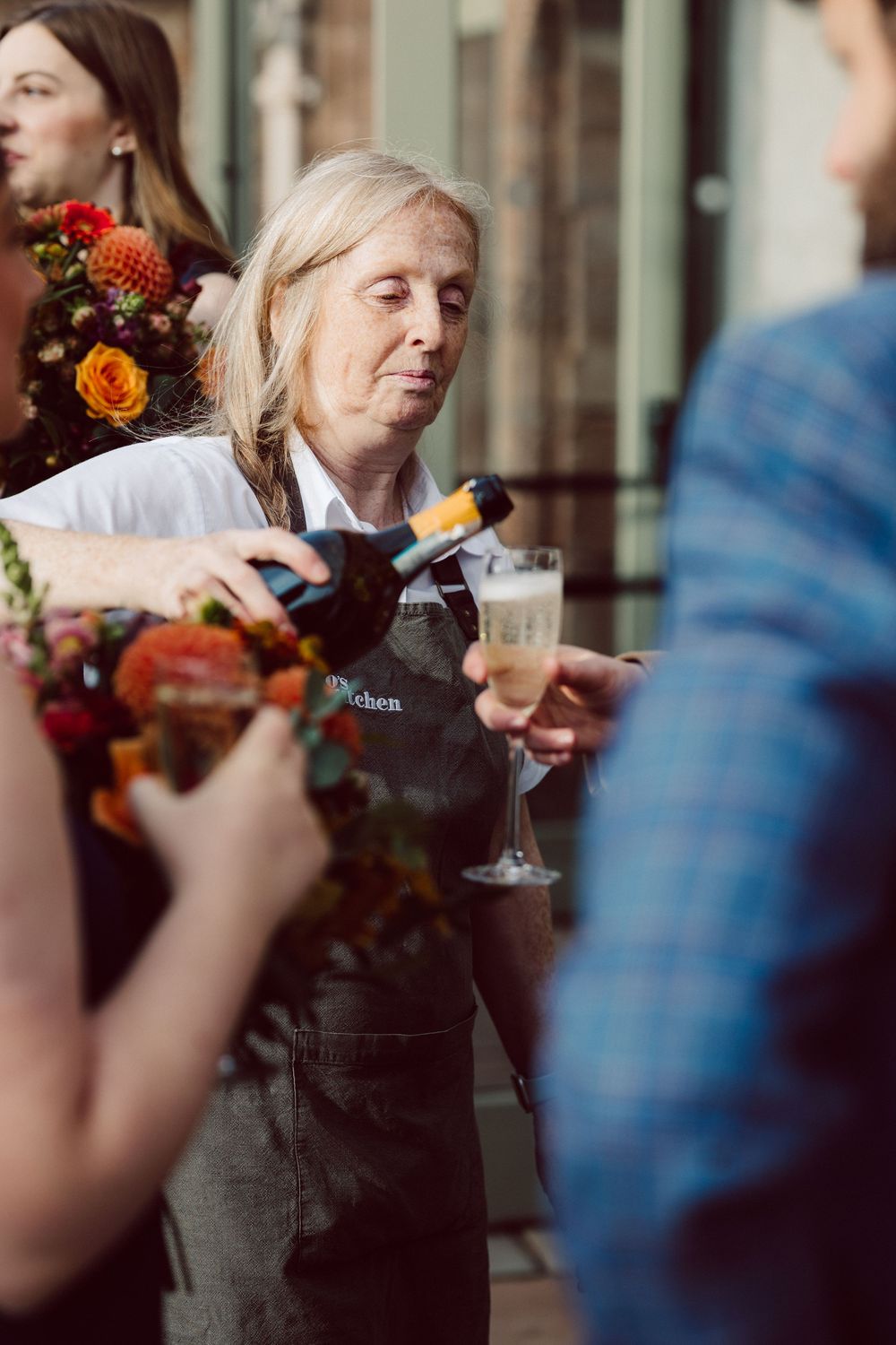 People enjoy cocktails and conversation at an elegant gathering with vibrant floral arrangements and warm lighting.