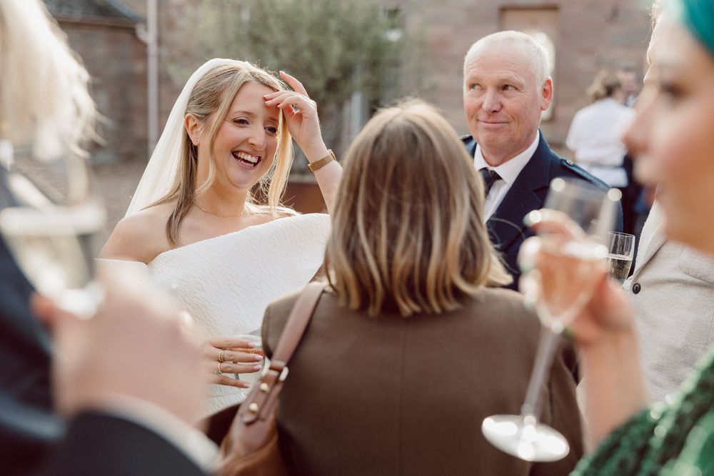 Wedding guests share laughter and champagne during an outdoor reception celebration.