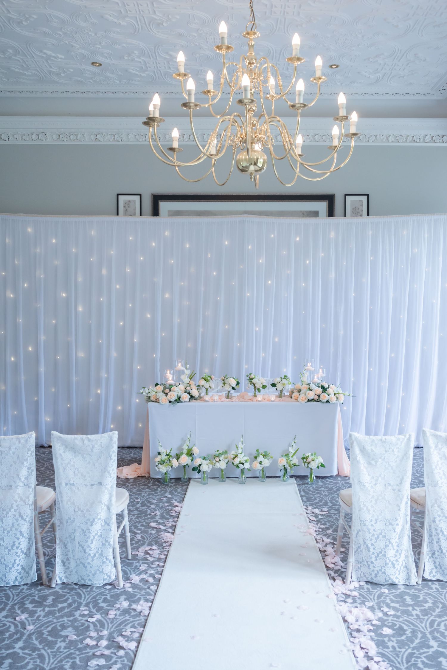 Elegant indoor wedding ceremony setup at De Vere Cranage Estate, Cheshire; featuring a romantic floral arch and crystal lighting