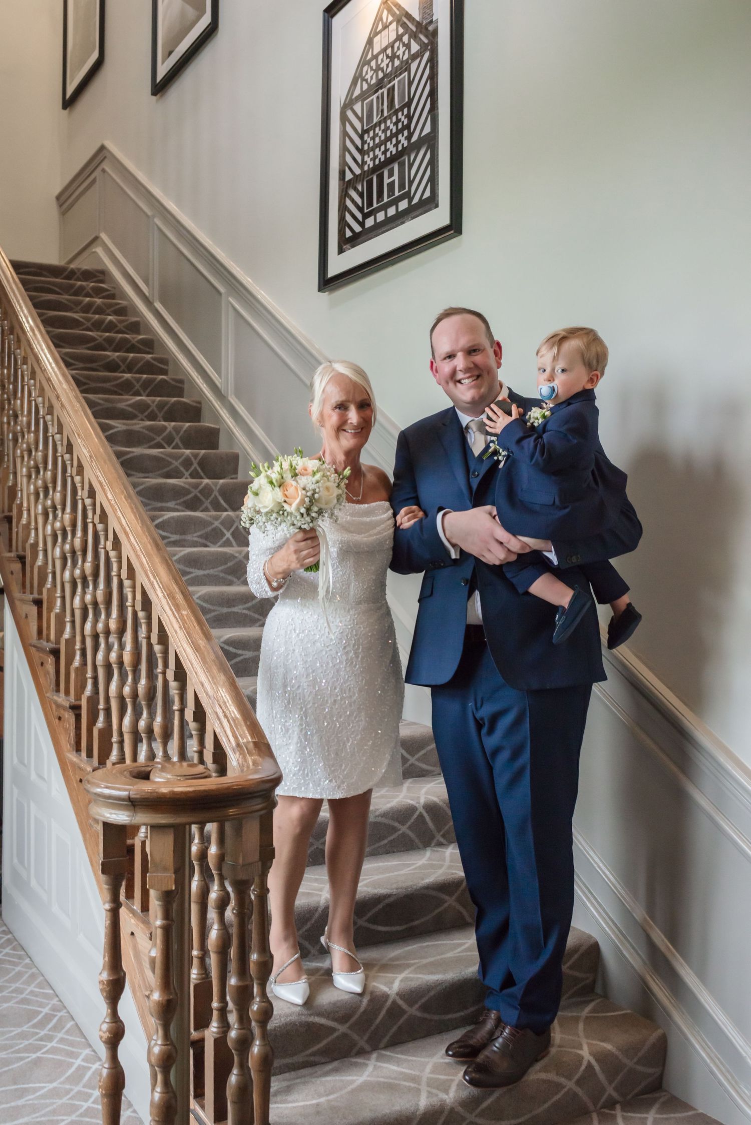 Three generations of a wedding party posing on the grand wooden staircase at De Vere Cranage Estate; wedding portraiture by Michael Pardoe
