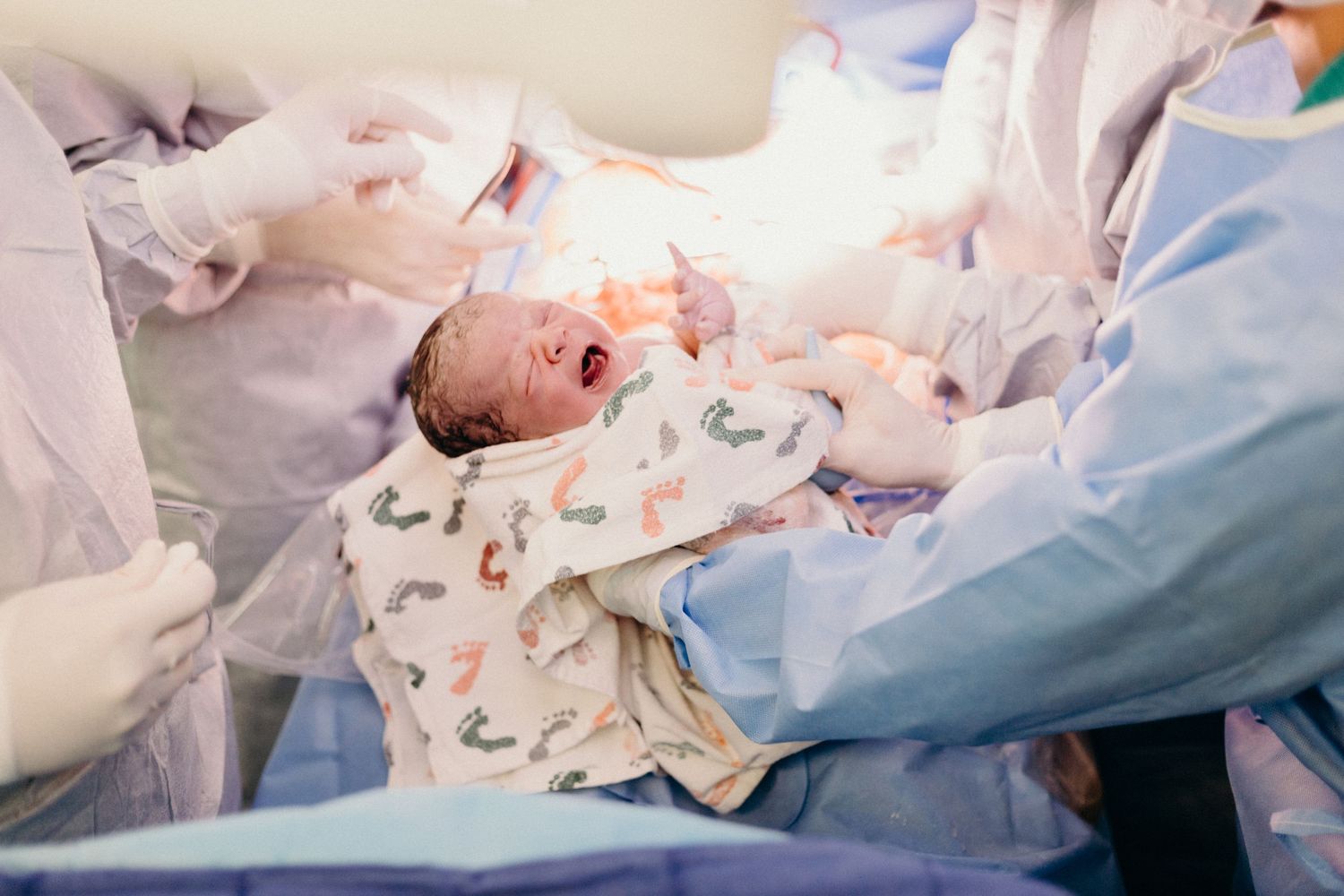 Medical team in protective gear attending to a newborn baby wearing a patterned onesie in a hospital setting.