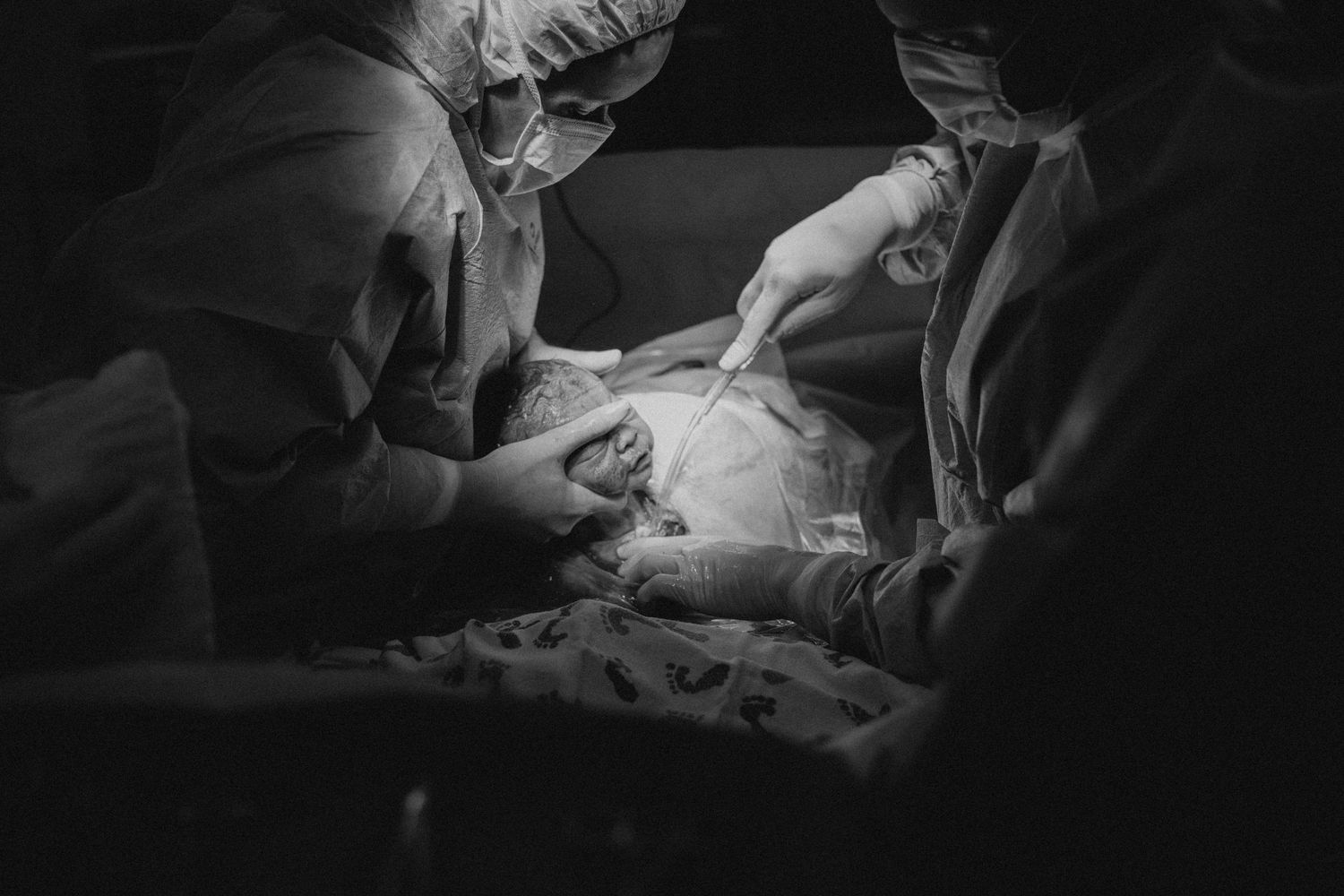 Medical professionals perform surgery in a dark operating room with focused lighting illuminating the surgical field.