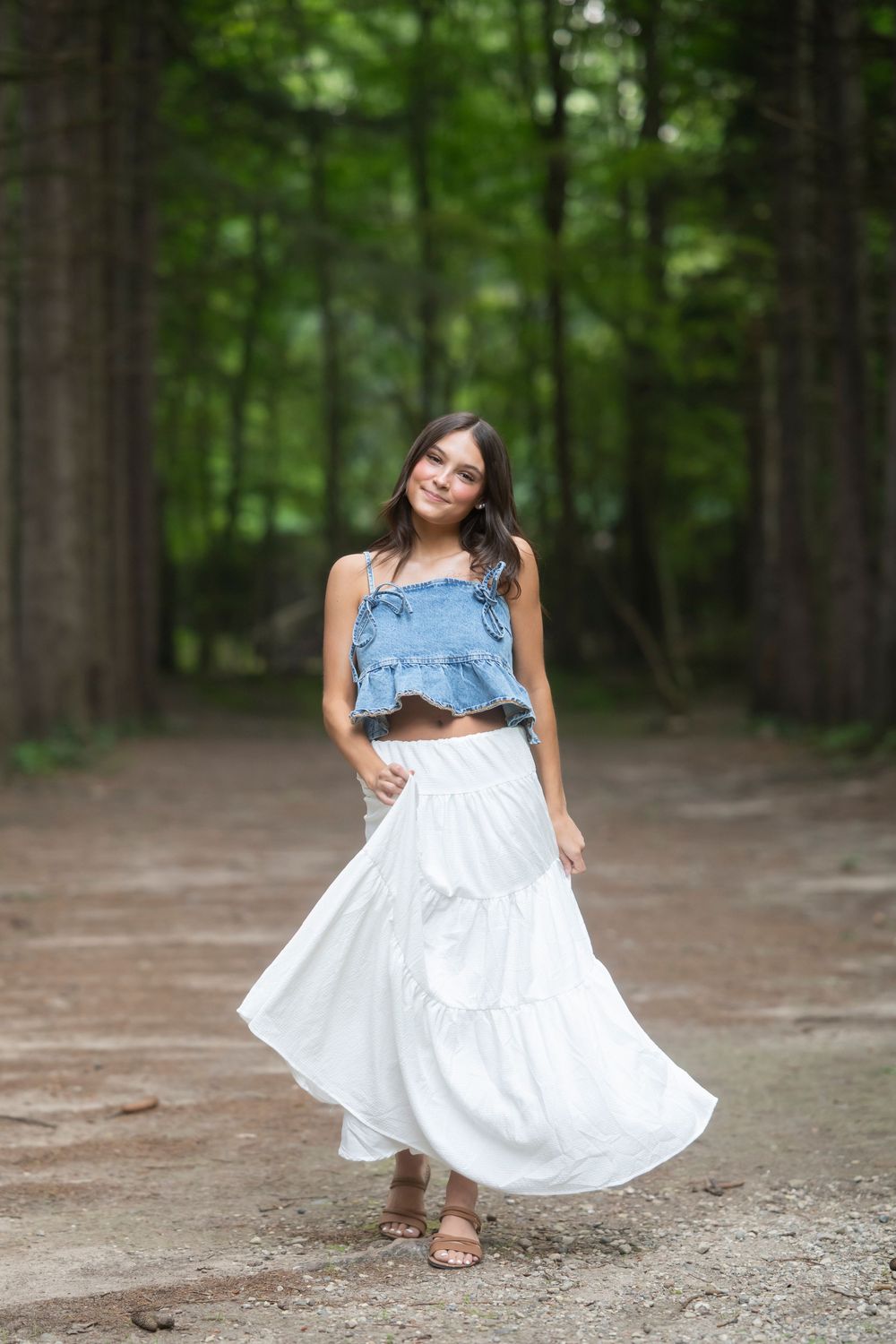 Denim crop top and flowing white skirt create movement along a forest path.