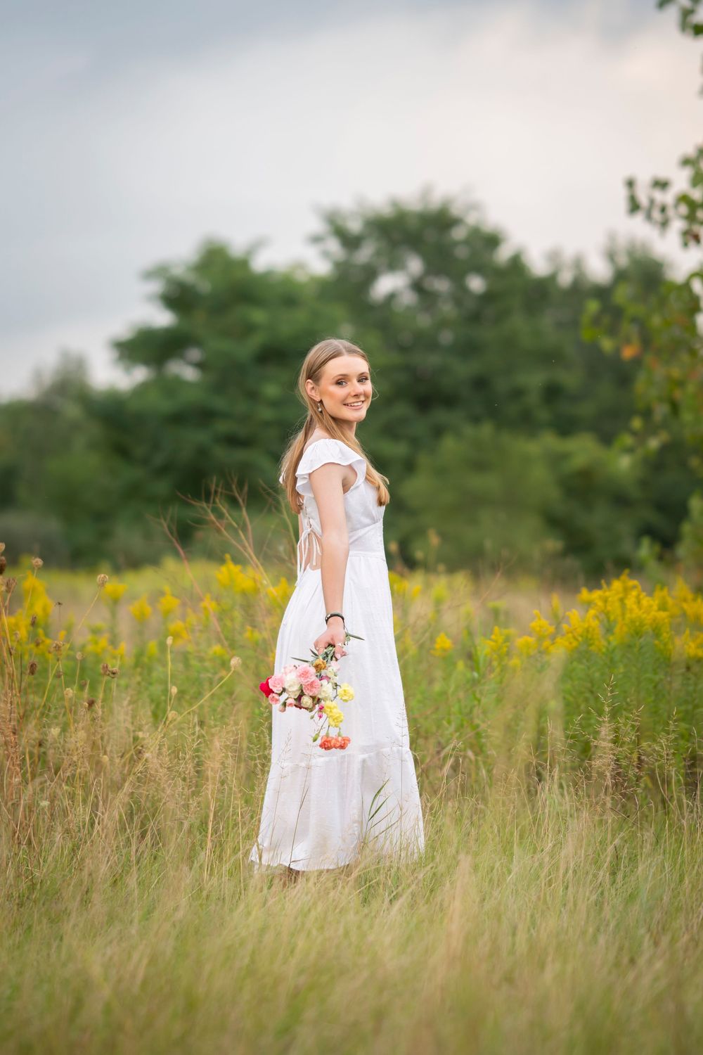 A white sundress flows in a summer meadow filled with yellow wildflowers during golden hour.