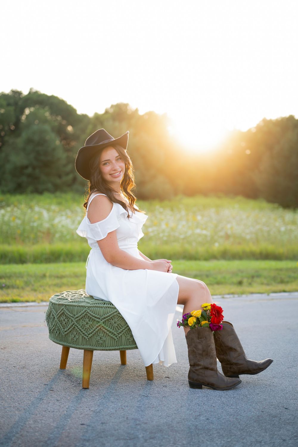 Western-inspired portrait with cowboy hat and boots on a tufted ottoman at sunset.