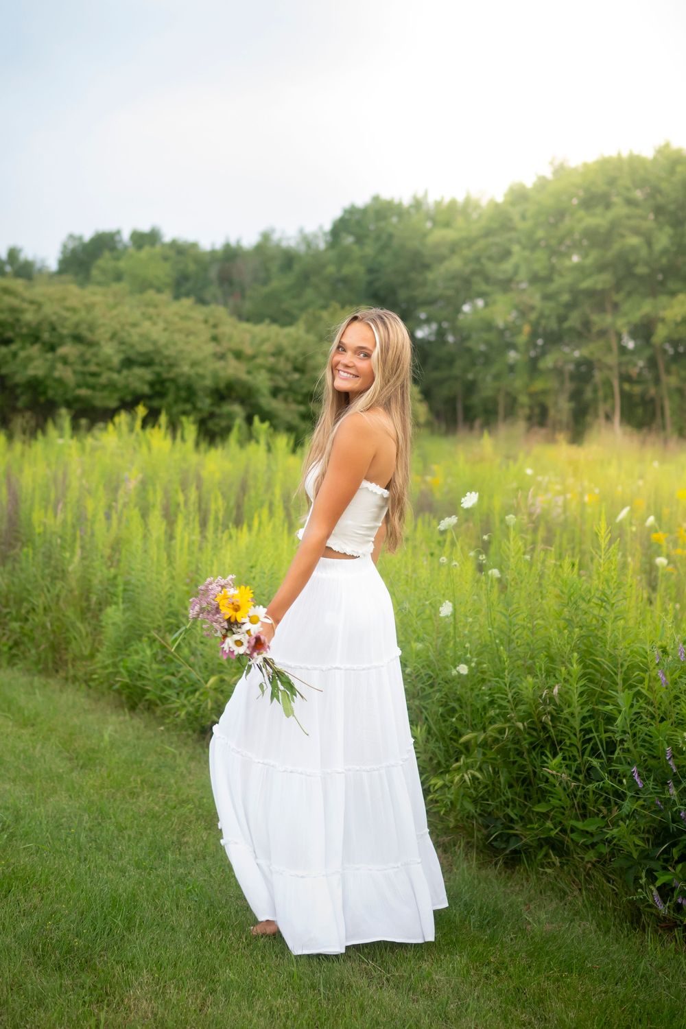 White summer dress twirls gracefully in a meadow filled with wildflowers and tall grass.
