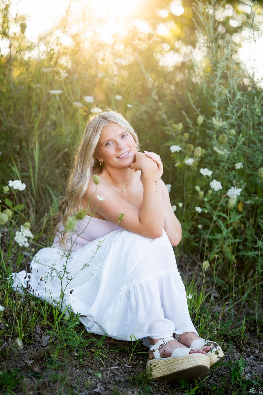 White dress creates ethereal contrast against wildflowers in golden sunset lighting.
