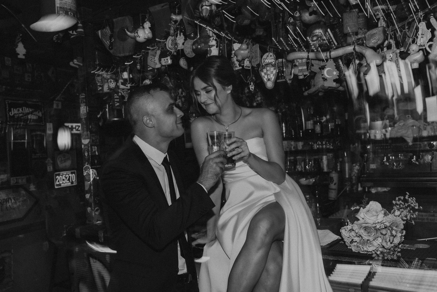 A black and white photo of a romantic moment at a vintage bar with bottles lining the wall.