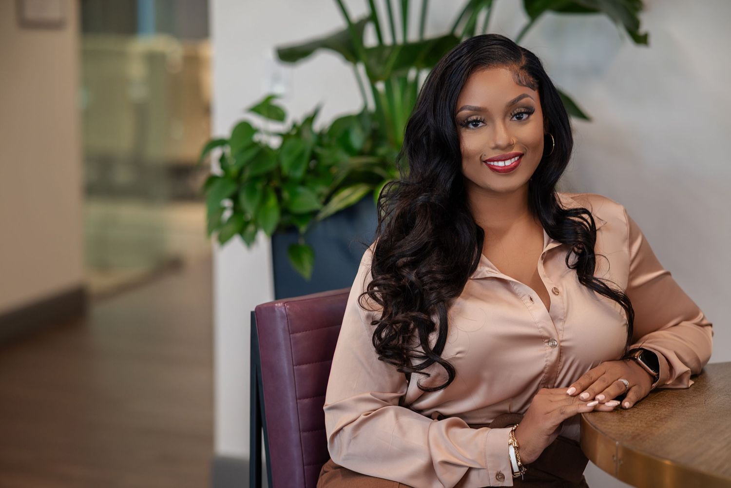 Professional woman in business attire sits at desk with laptop and documents in modern office setting.