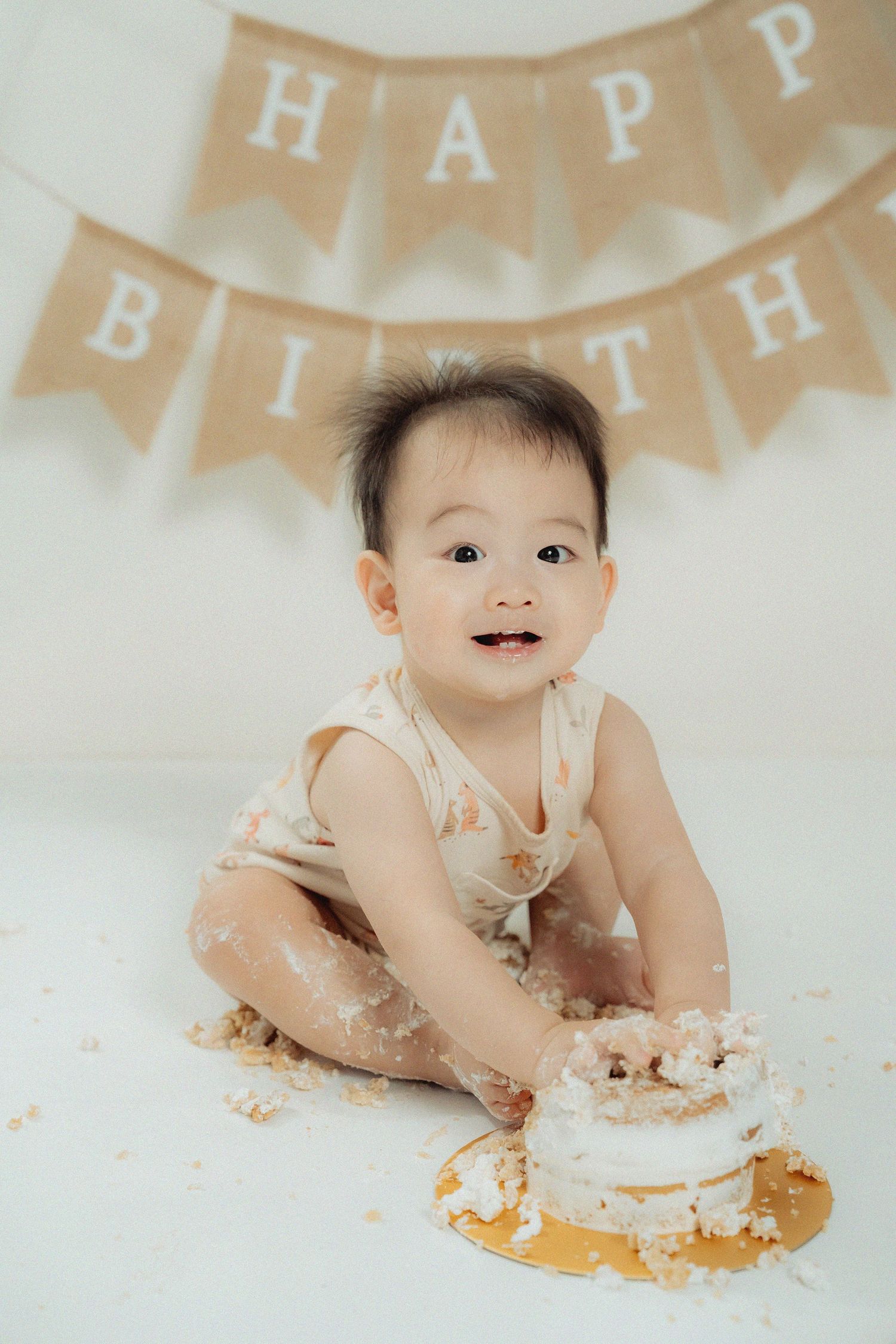 Baby's first birthday cake smash photo session with beige bunting decoration.
