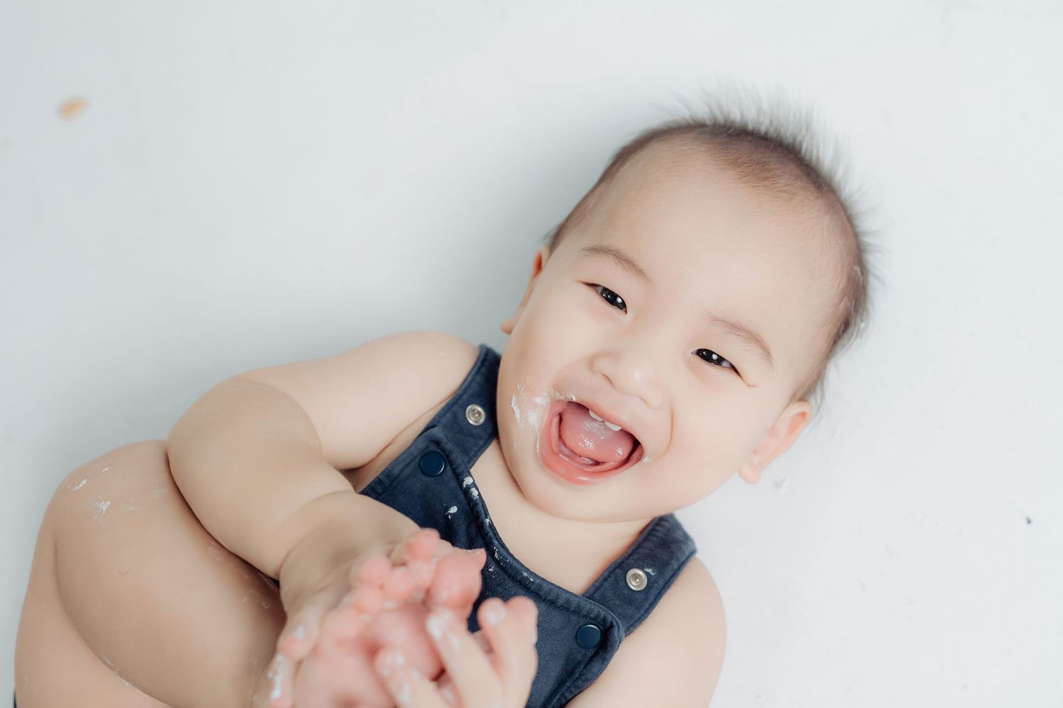 Baby wearing navy outfit playing on white floor during birthday photoshoot.