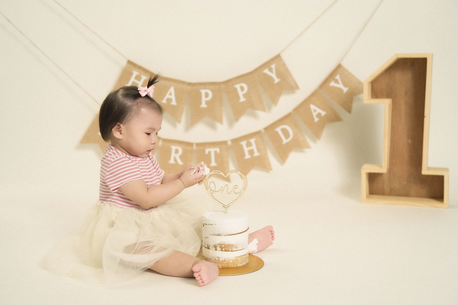 First birthday cake smash setup with neutral colors and decorative banner.