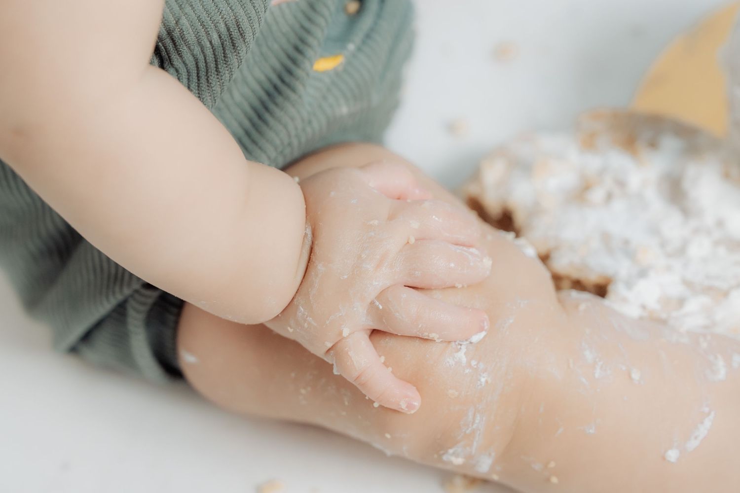 Small hands covered in white flour kneading dough on a light colored surface.