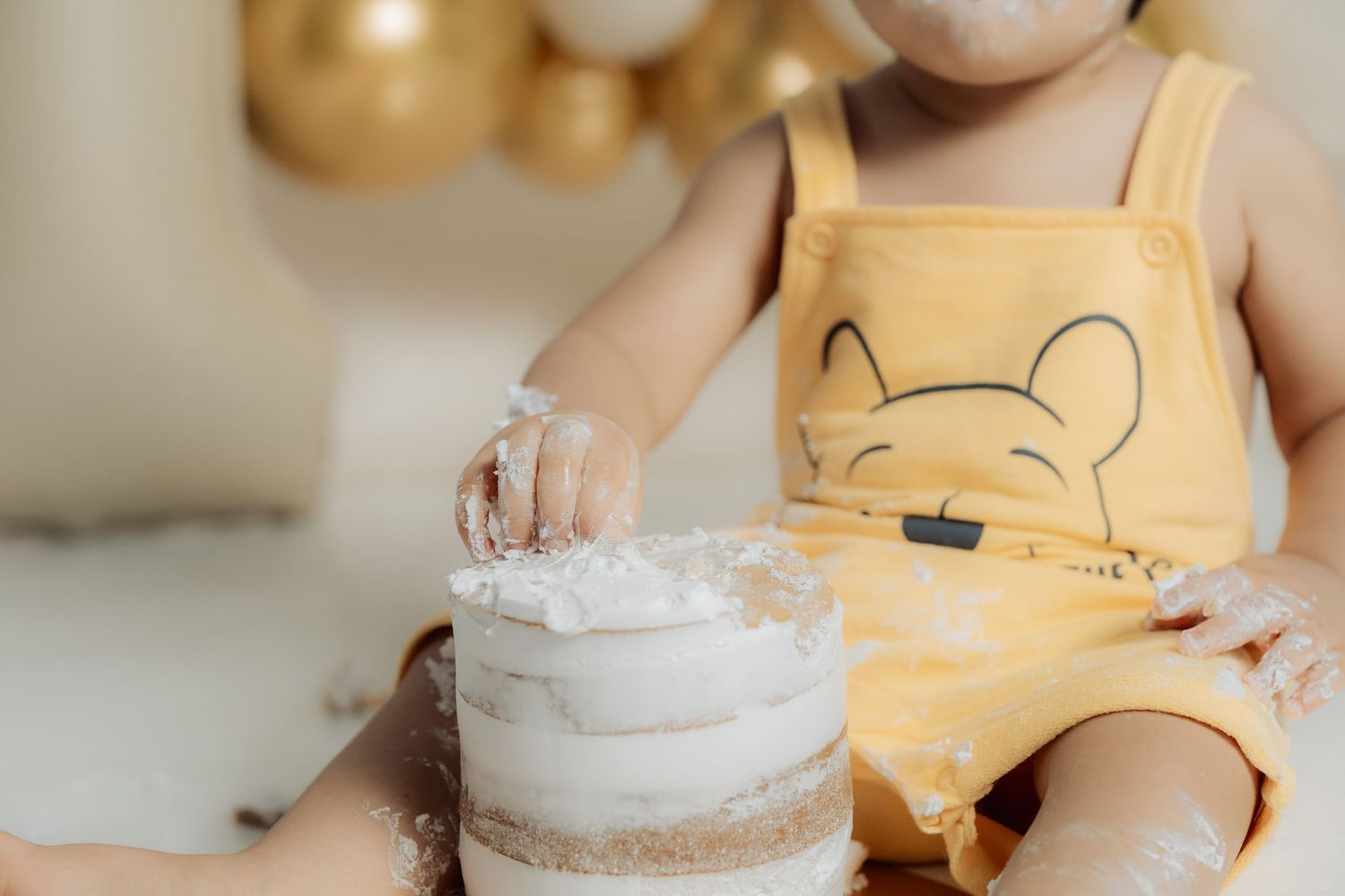 First birthday cake smash session with white frosted cake and gold decorations.