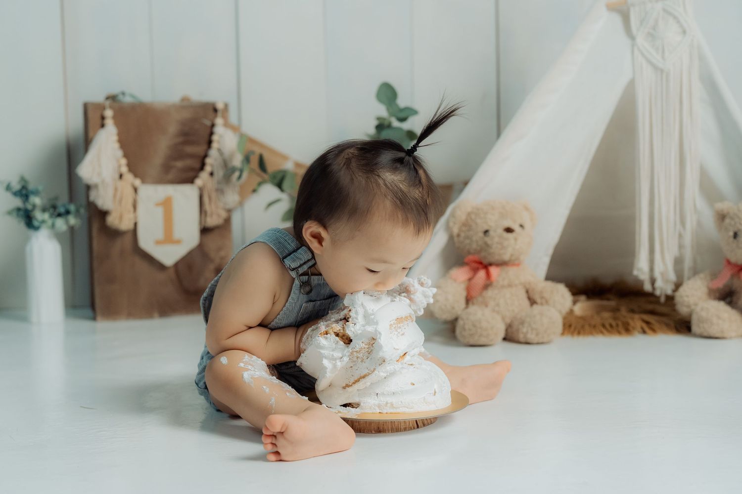 Baby in white outfit exploring and playing with toys near a teepee tent and stuffed animals.