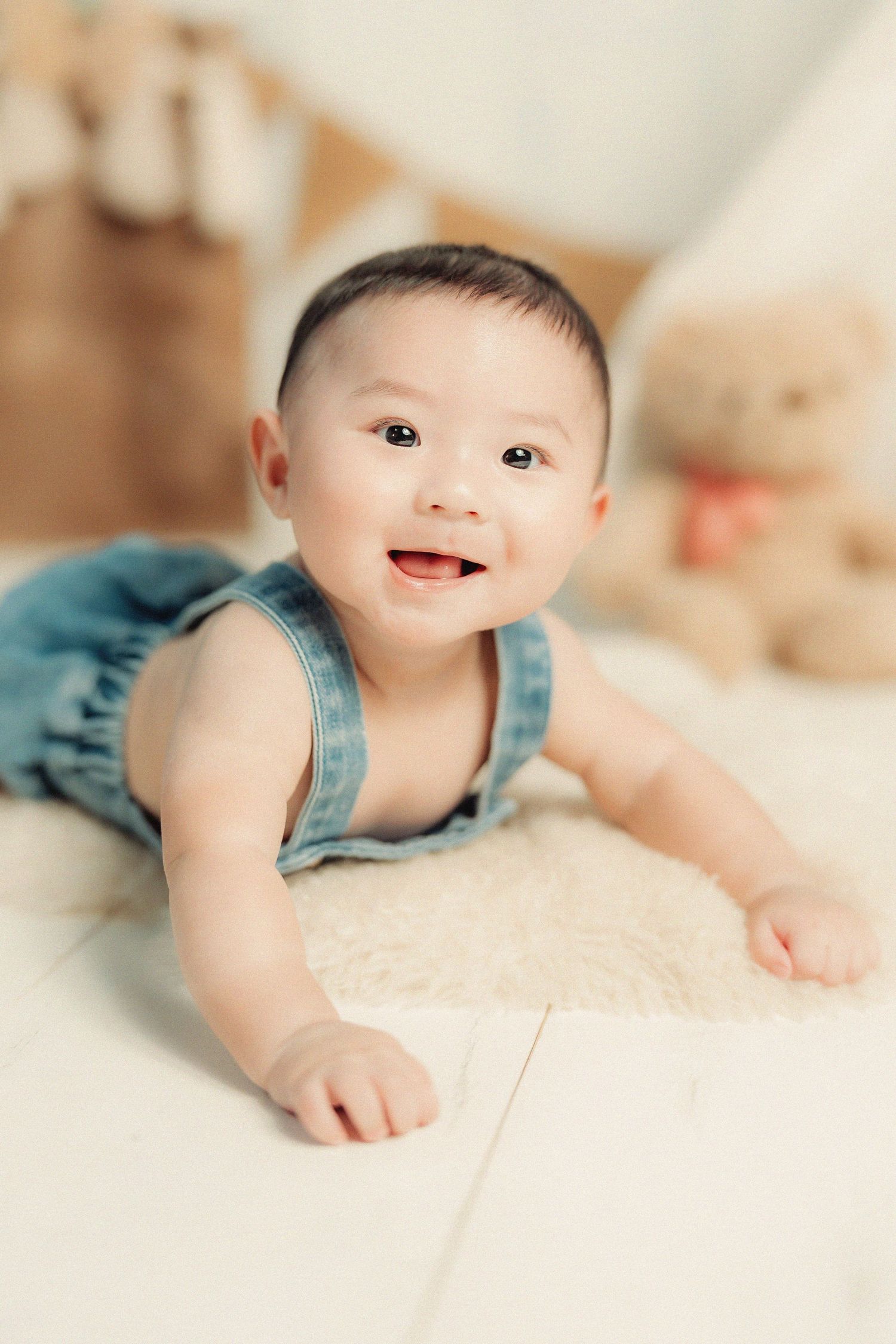 Baby in denim romper lying on cream blanket during portrait session.