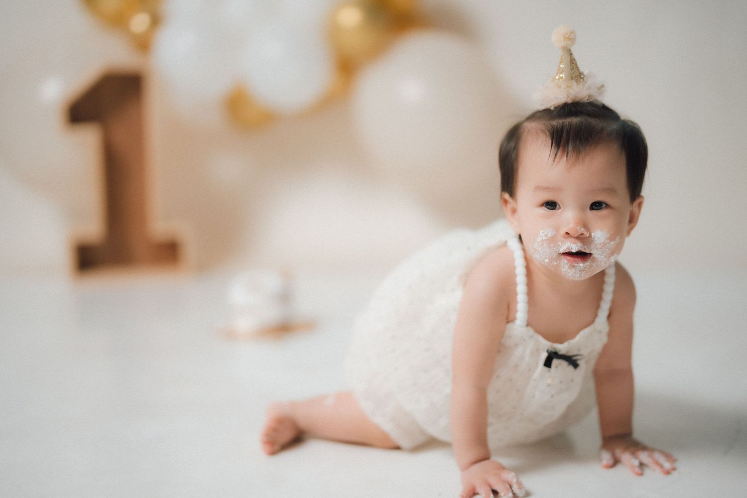 Baby crawling during first birthday photoshoot with gold and white balloons.