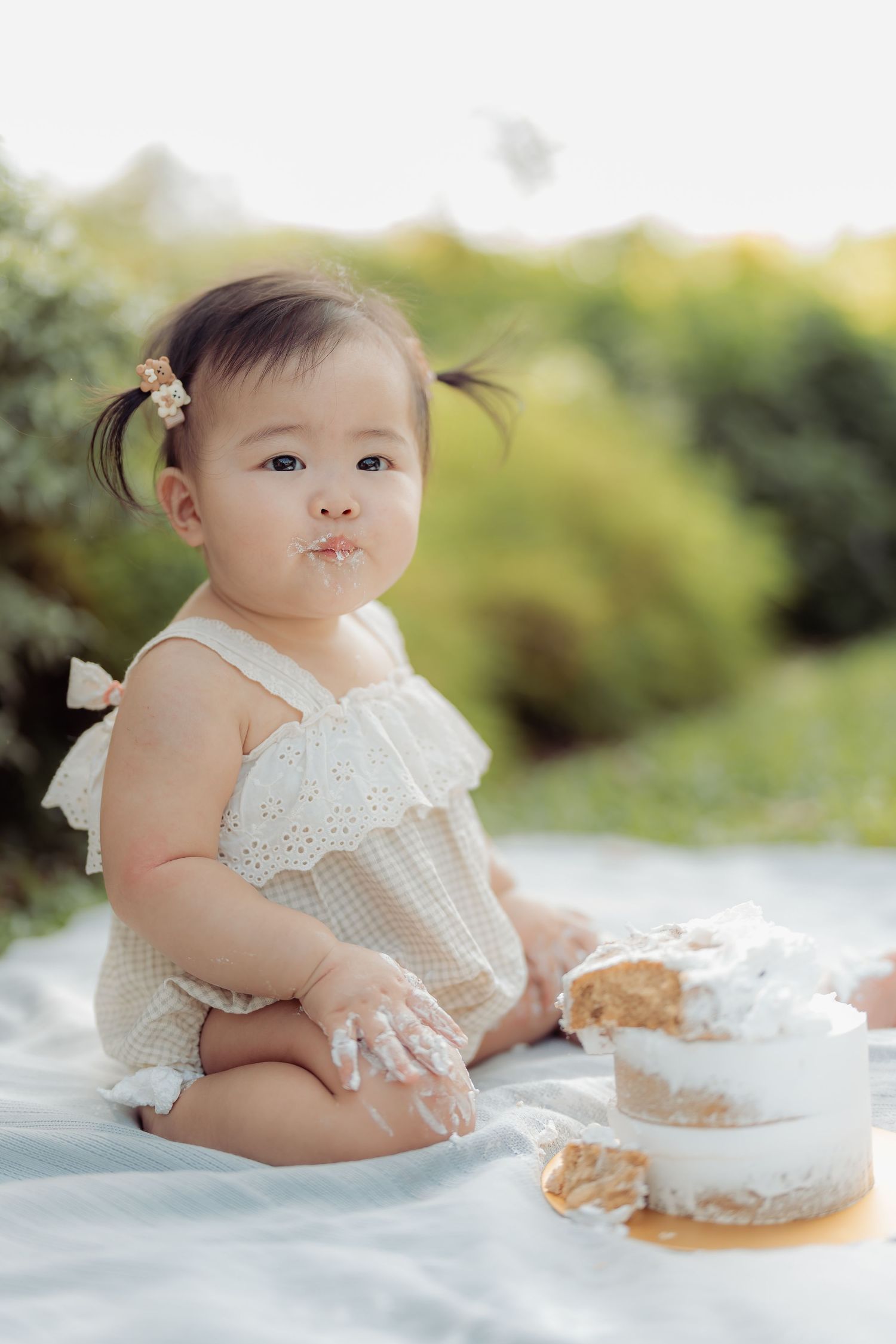 Baby in white lace dress having outdoor cake smash photo session.