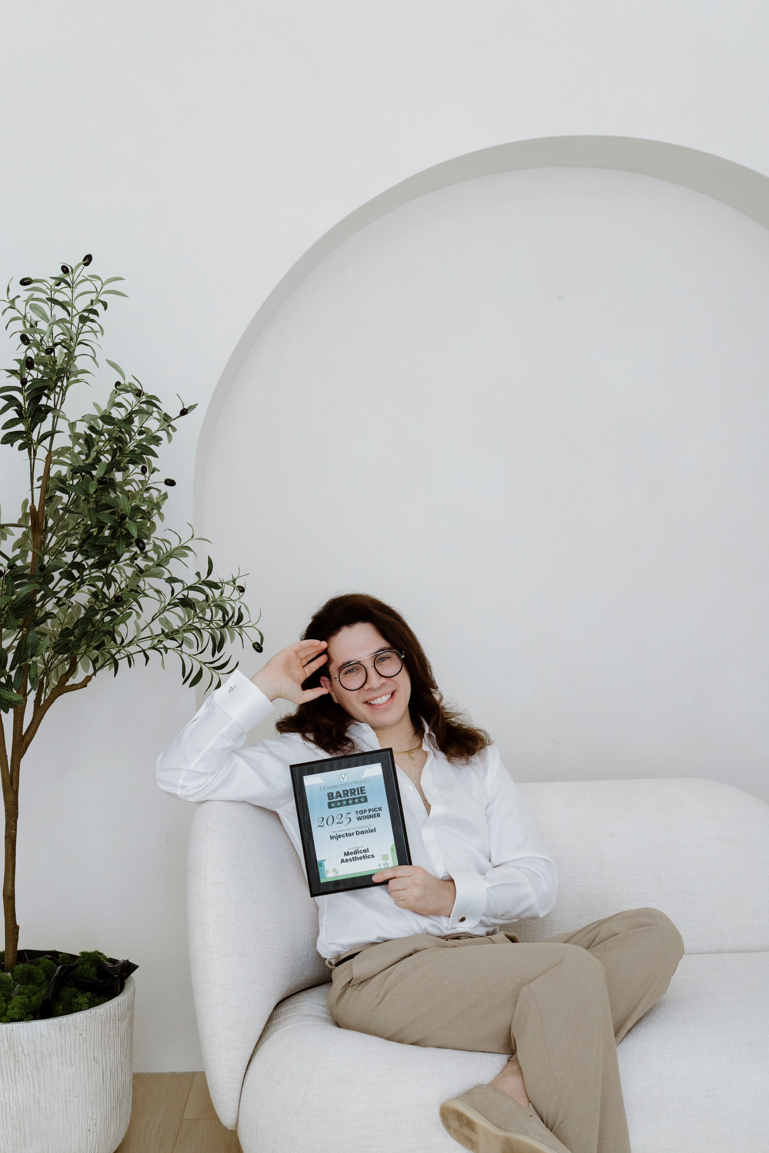 Person relaxing on white couch with digital device and decorative plant in minimalist setting.