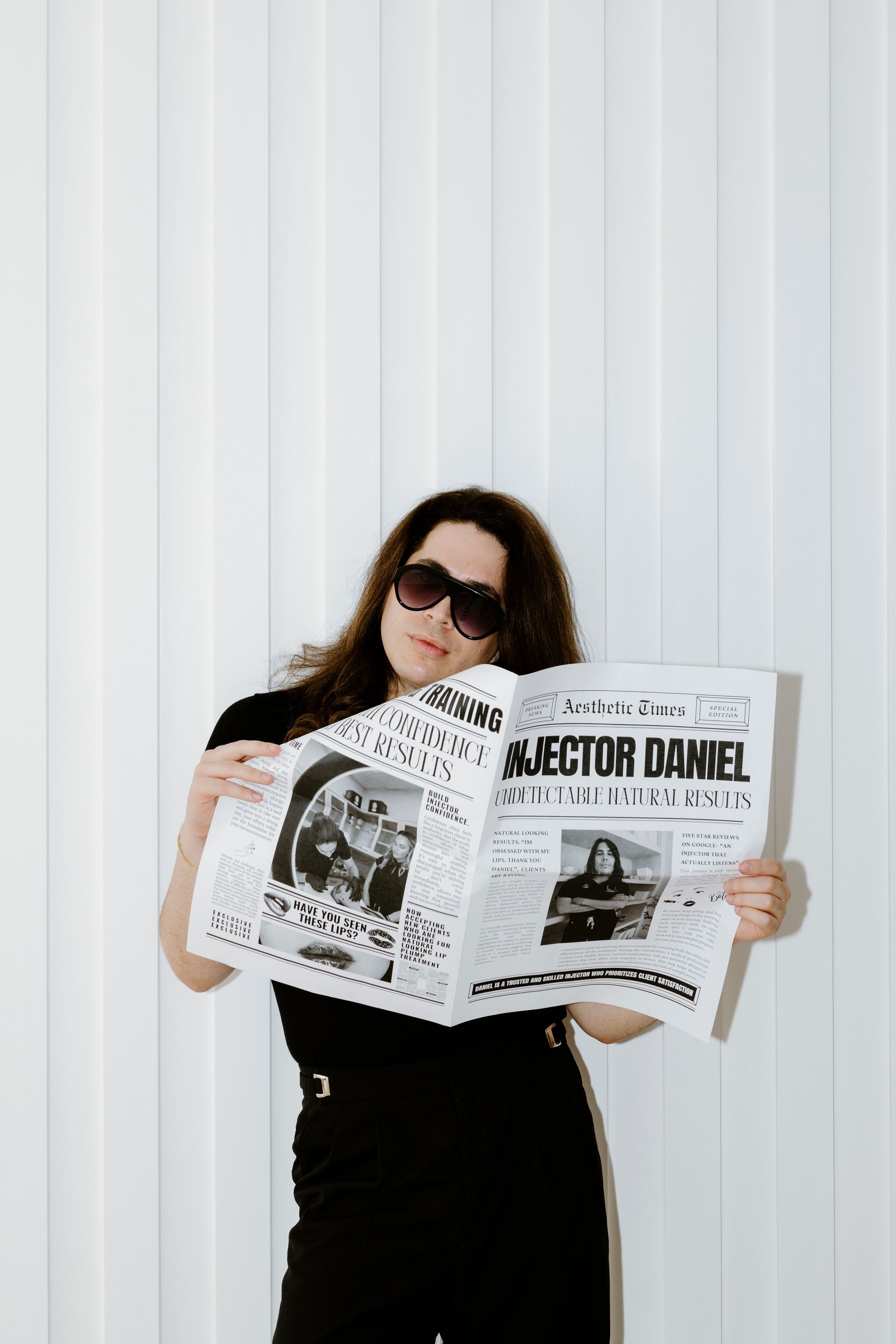 Professional wearing black suit reads newspaper in bright white studio setting.